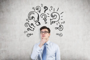 Young businessman attacked by aggressive question mark images on concrete wall. Concept of too many questions. Mock up