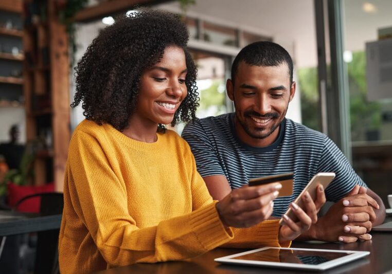 smiling woman entering credit card details on a laptop with her boyfriend watching