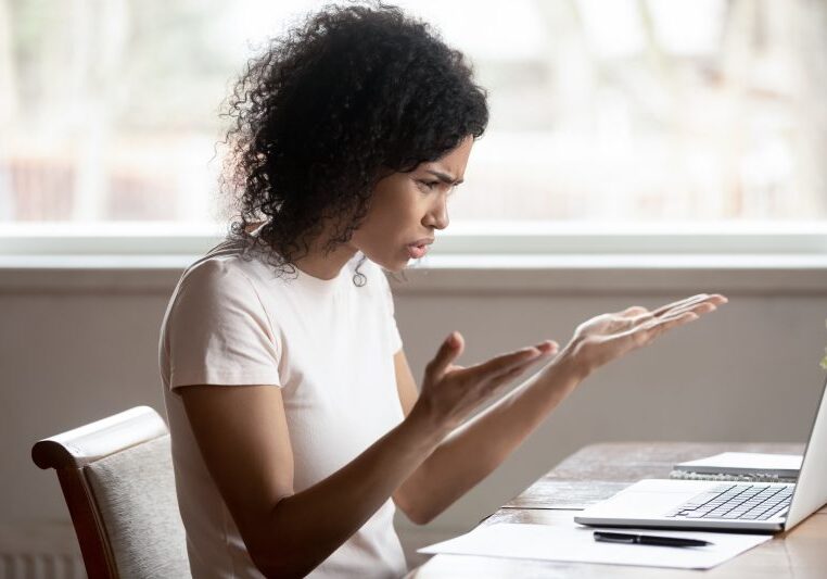curly haired woman with a frustrated expression gesturing with her hands at her laptop
