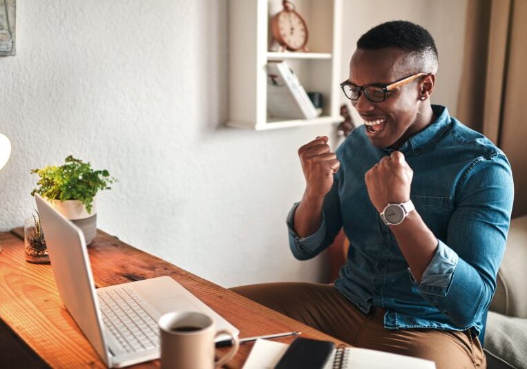 young businessman sitting alone in his home office and feeling excited while using his laptop