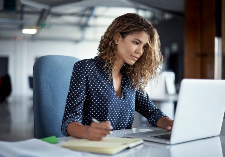 Cropped shot of a young businesswoman making notes while working on a laptop in a modern office