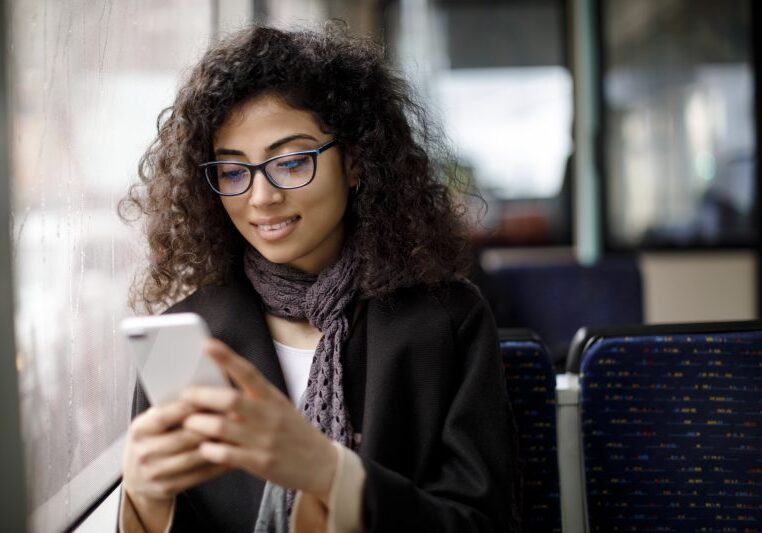 Smiling young woman traveling by bus and using smart phone